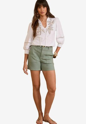 White blouse with embroidered leaf patterns and long puff sleeves, paired with olive green shorts, showcasing pockets and a high waist.