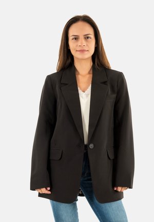 Blazer nero su misura con revers a punta, chiusura a un bottone e due tasche frontali, indossato su un top bianco e jeans in denim.