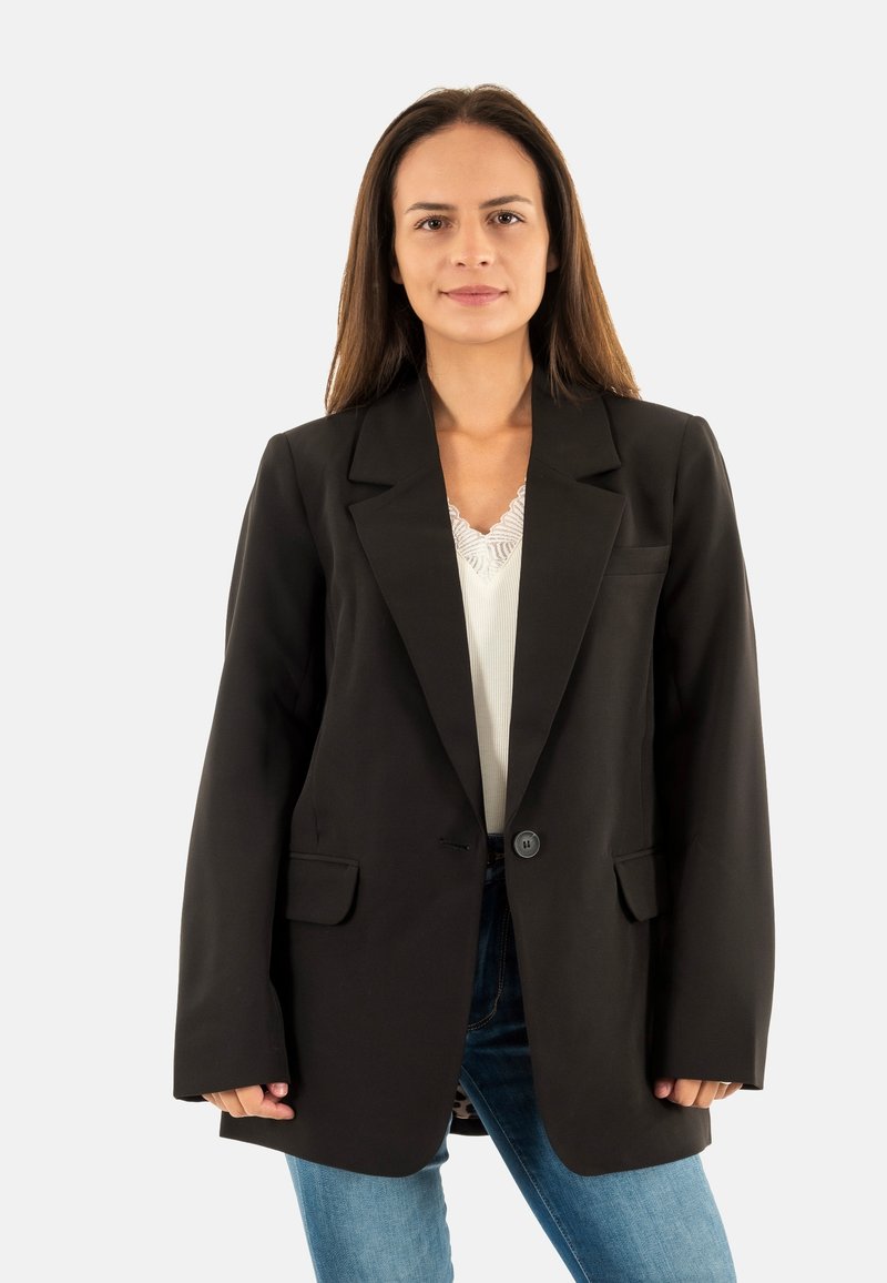 Blazer noir ajusté avec un revers cranté, fermeture à un bouton, et deux poches avant, porté sur un haut blanc et un jean en denim.