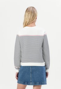 Witte sweatshirt met marineblauwe en rode horizontale strepen op de rug, gecombineerd met een spijkerrokje, met ribgebreide manchetten en onderrand.