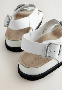 Sandali bianchi con tomaia in pelle liscia, fibbia regolabile e soletta imbottita; suola in gomma nera, design piatto con decorazioni minime.