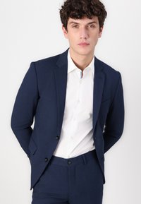 Marineblauer maßgeschneiderter Anzug mit einem eleganten Design, bestehend aus einem einreihigen Sakko, passenden Hosen und einem weißen Hemd darunter.