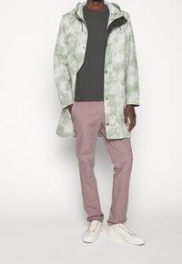 Jasnopłaszczowy płaszcz przeciwdeszczowy w kolorze jasnozielonym z kapturem, pod spodem szara koszula i bladoróżowe spodnie. Całość dopełniają białe trampki z wielokolorowymi oczkami.