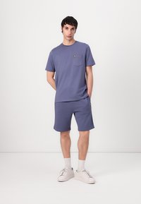 Lys lilla bomull t-skjorte med korte ermer og brystlomme, kombinert med matchende shorts. Begge har en liten gul logo detalj.