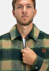 Gestreepte wollen jas in tinten van groen en beige, met een ritssluiting aan de voorkant, een kraag en een leren merkpatch op de borst.