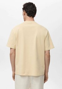 Tricou cu manșă scurtă din bumbac bej deschis, croială obișnuită, cu decolteu rotund și textură netedă. Design simplu, fără modele sau accente.