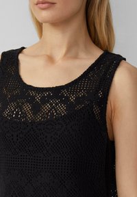 Zwarte gebreide tanktop met een ronde hals, een ingewikkeld kantpatroon en een gestructureerde stof. Het ontwerp bevat verschillende steekpatronen.