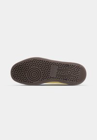 Semelle de chaussure en caoutchouc brun foncé avec un motif de bande de roulement circulaire et logo Puma sur un fond clair uni.
