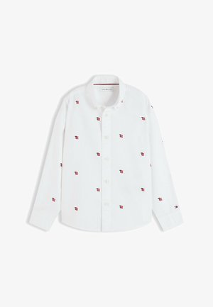 Hvid skjorte med lange ærmer med små røde og sorte "TH" logoer broderet over det hele og et Tommy Hilfiger-flag på venstre manchet.