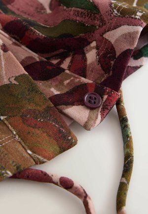 Auduma ar ziedu rakstu zemes toņos - zaļā, sarkanā un rozā; ar mīkstu faktūru un bordoviešu pogu malā.