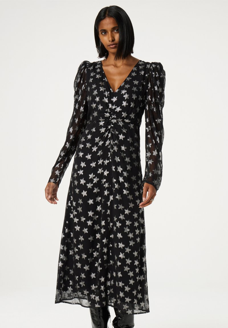 Schwarzes Kleid mit durchsichtigen, puffartigen langen Ärmeln, das ein Sternmuster in Silber aufweist. Das Kleid hat einen V-Ausschnitt und eine geraffte Taillenpartie.