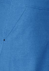 Blå tyg, lätt texturerad, med vinklade sömmar och en synlig svart tryckknappdetalj. Ren design med sydda accenter.