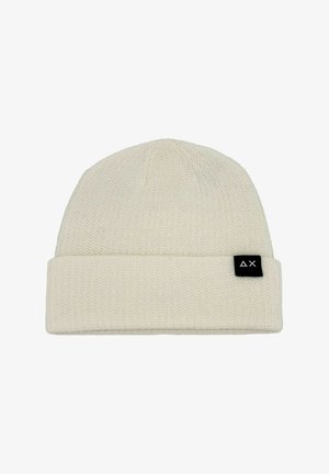 Beanie lavorato a maglia in beige chiaro, caratterizzato da un risvolto e un piccolo etichetta nera con un logo bianco sul lato. Texture morbida e design semplice.