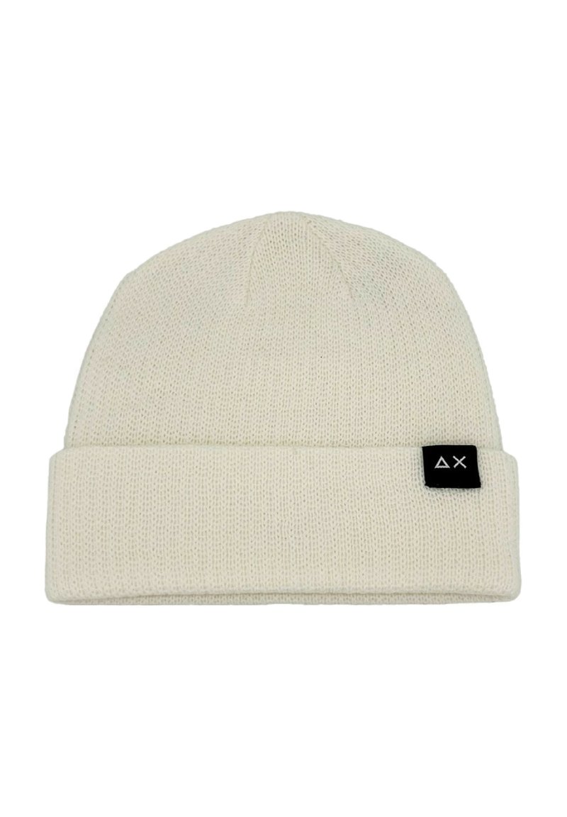 Beanie lavorato a maglia in beige chiaro, caratterizzato da un risvolto e un piccolo etichetta nera con un logo bianco sul lato. Texture morbida e design semplice.