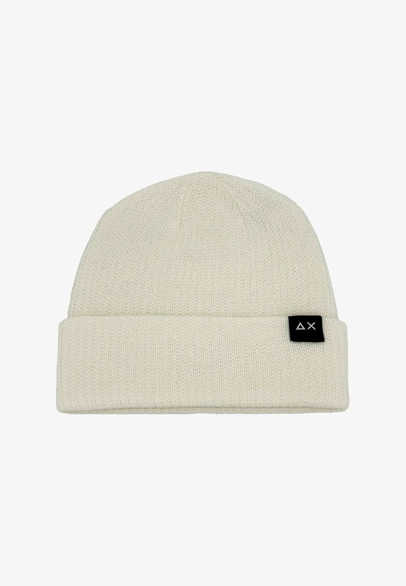 Beanie lavorato a maglia in beige chiaro, caratterizzato da un risvolto e un piccolo etichetta nera con un logo bianco sul lato. Texture morbida e design semplice.
