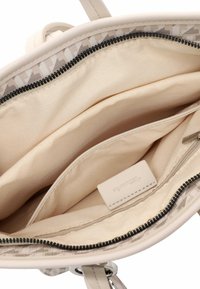 Intérieur d'un sac fourre-tout beige avec une doublure en tissu lisse, une poche zippée et une étiquette. L'intérieur comprend plusieurs compartiments pour une meilleure organisation.