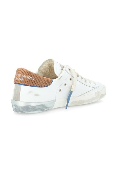 Sneaker bianco con tallone in corduroy marrone testurizzato, accenti blu e suola in gomma trasparente. Presenta una pelle liscia e graffiata per un contrasto.