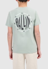 lichtgroene katoenen t-shirt met een grote zwarte cirkelvormige grafiek met herhaaldelijke tekst "BALLIN" op de achterkant en korte mouwen.