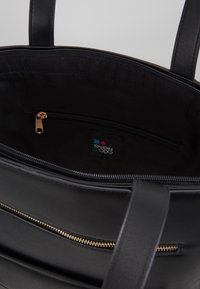 Intérieur en cuir noir avec une poche zippée. Détails en zip doré et un patch avec logo. Texture lisse, design spacieux.