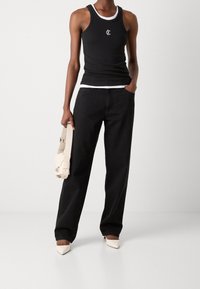 Svart linne med vit kant, logotyp på bröstet; höga, löst sittande svarta jeans; håller en gräddfärgad handväska; bär spetsiga beiga klackar.