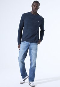 Marineblauses Hemd mit strukturiertem Muster, kombiniert mit hellblauen geraden Jeans und weißen Sneakern mit schwarzen Streifen.