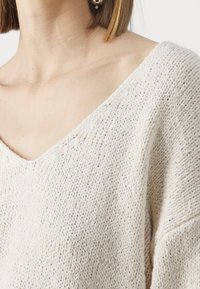 Lichtbeige gebreide trui met een V-hals, textuurstof en een losse pasvorm. Zichtbare stiksels verbeteren het algehele ontwerp.