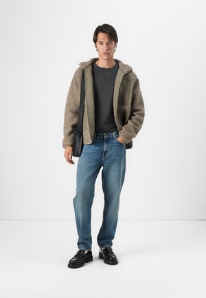 Chaqueta de forro polar marrón con forro verde, camisa gris, vaqueros azules y zapatos negros. Corte slim, detalles de bolsillos y diseño casual.
