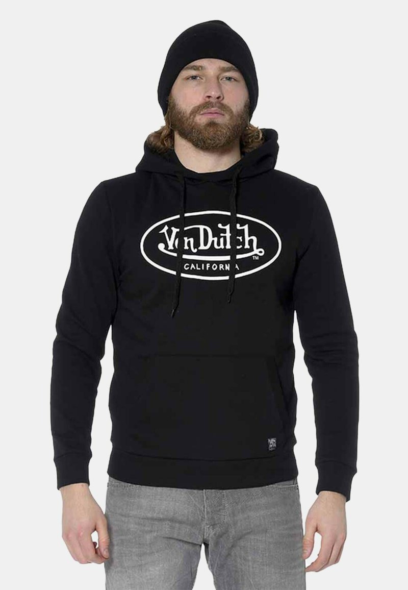 Sudadera negra de algodón, con un logo blanco en la parte frontal, cordones y un bolsillo delantero. Combinada con jeans gris claro.