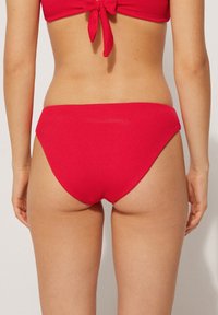 Bas de bikini rouge en tissu texturé, présentant un design taille haute avec une couleur unie et des bords lisses.