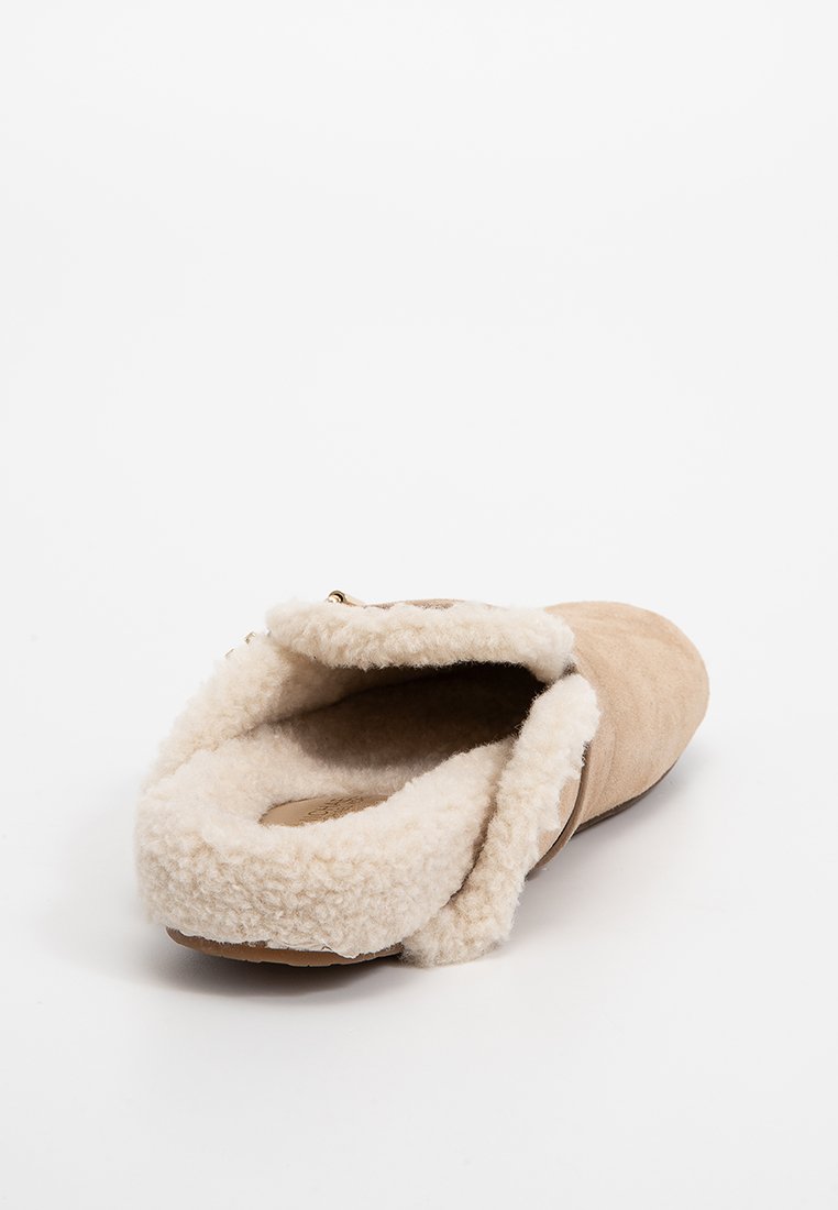 Pantoufle en daim beige avec une doublure en polaire crème douce et un dos légèrement surélevé. Présente un bout arrondi et un matériel minimal.