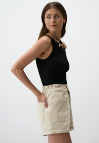 Body suit nero senza maniche con texture a costine abbinato a pantaloni corti in lino beige a vita alta con una vita arricciata e tasche laterali.