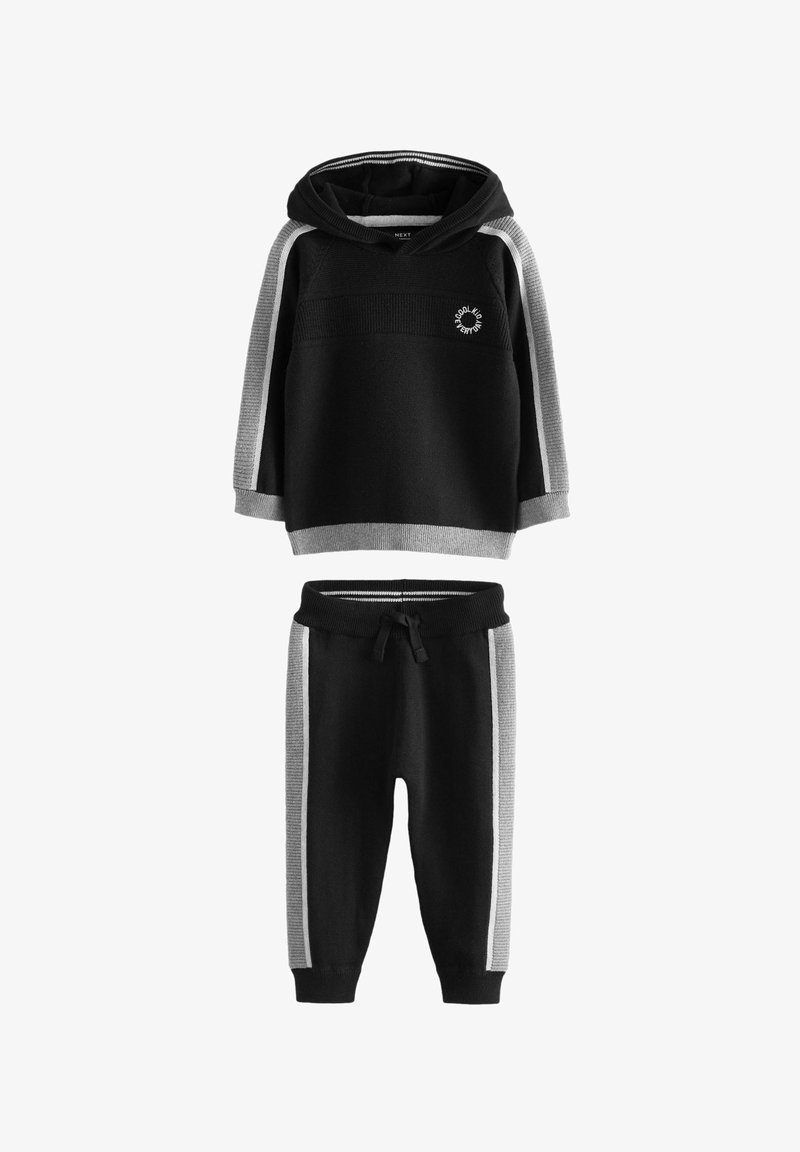 Fekete kapucnis pulóver szürke kiegészítőkkel és logóval, fekete melegítőnadrággal párosítva, amely szürke oldalsávokkal rendelkezik. Puha anyag, laza fazon.