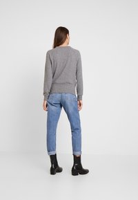 Szary sweter z ściągaczami przy rękawach i dolnym brzegu, w połączeniu z jasnoniebieskimi dżinsami podwiniętymi u dołu, noszony z czarnymi botkami za kostkę.