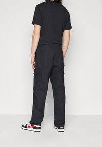 Svart avslappnad t-shirt och cargo-byxor med flera fickor, rak ben, och en slät, vävd textur. Svart och vit sneakers med röda accenter.