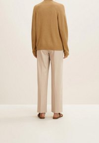 Suéter de punto color canela combinado con pantalones de pierna ancha beige claro y sandalias marrones, visto desde atrás contra un fondo claro.
