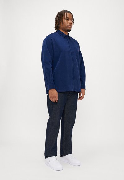 Μπλε κονδύλι πουκάμισο με σχέδιο κουμπώματος, συνδυασμένο με σκούρα τζιν παντελόνια και λευκά αθλητικά παπούτσια. Διαθέτει τσέπη στο στήθος και μακριά μανίκια.