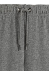 Szare dresy z elastycznym pasem w talii i sznurkiem do regulacji. Tkanina jest miękka o gładkiej fakturze, z metalowymi oczkami do sznurków.