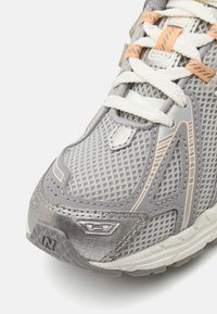 Baskets de sport grises avec une tige en maille, des accents texturés et des détails orange. Comprend des lacets blancs et un col rembourré pour le soutien.