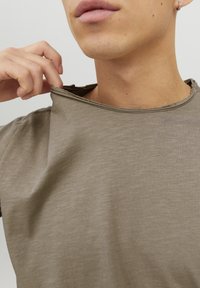 Camiseta verde oliva de manga corta hecha de algodón suave y texturizado; presenta un borde sin pulir alrededor del cuello y un corte relajado.