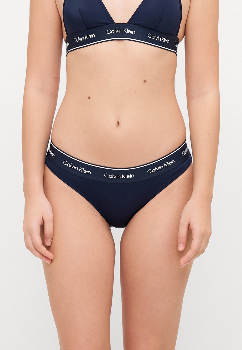Námornícka modrá podprsenka a bikiny Calvin Klein, s hladkou tkaninou a pásom s logom. Podprsenka má trojuholníkový dizajn.