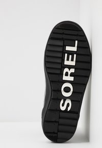Czarna gumowa podeszwa buta z głębokimi bieżnikami, wytłoczone logo "SOREL" oraz teksturowaną powierzchnią dla lepszej przyczepności.
