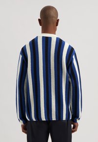 Paksu neulepusero, jossa pystysuorat raidat sinisessä, mustassa ja kermanvärisessä. Löysä malli, pitkät hihat ja resorit hihansuissa. Kuvioitu kangas.