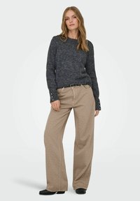 Tamno siva pletena dukserica sa širokim rukavima, u kombinaciji s svijetlosmeškim hlačama širokih nogavica sa bijelim točkicama i crnim pojasom. Crne cipele.