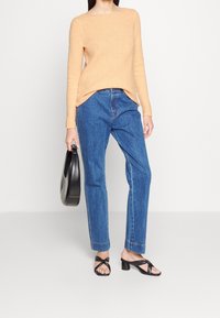 Helles orange gestricktes Sweatshirt, blaue gerade Jeans, schwarze Riemchen-Absatzsandalen und eine kleine schwarze Handtasche.