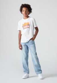 Valge puuvillane T-särk, millel on oranž ja sinine "Levi's" graafika. Koos helesiniste teksade ja valgete tossudega.