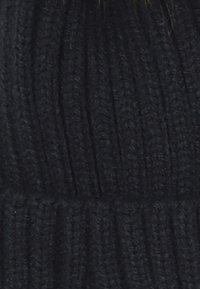 Beanie nero lavorato a maglia con texture a coste, filato spesso e vestibilità aderente, adatto per il freddo. Nessun motivo o decorazione visibile.