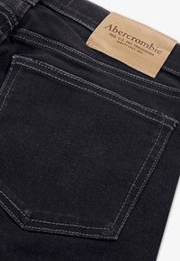 Jeans de mezclilla negra con una etiqueta de cuero que muestra el texto "Abercrombie", detalles de costura visibles en el bolsillo trasero y una textura suave.
