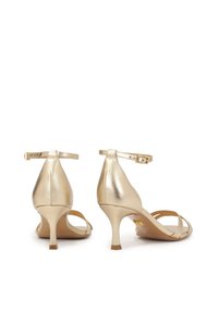 Gold metallic heeled sandals with a pointed toe, ankle straps, and a slender heel. Smooth texture with minimalistic design accents.