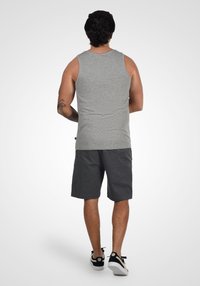 Camiseta sin mangas gris de textura suave, combinada con pantalones cortos oscuros. Los pantalones cortos tienen una tela ligeramente texturada y son de longitud hasta la rodilla. Zapatillas negras.
