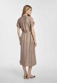 Midi-długości brązowa sukienka z gładkiego materiału, z podwiniętymi rękawami i materiałowym paskiem. Posiada rozcięcie z tyłu, co ułatwia ruchy.